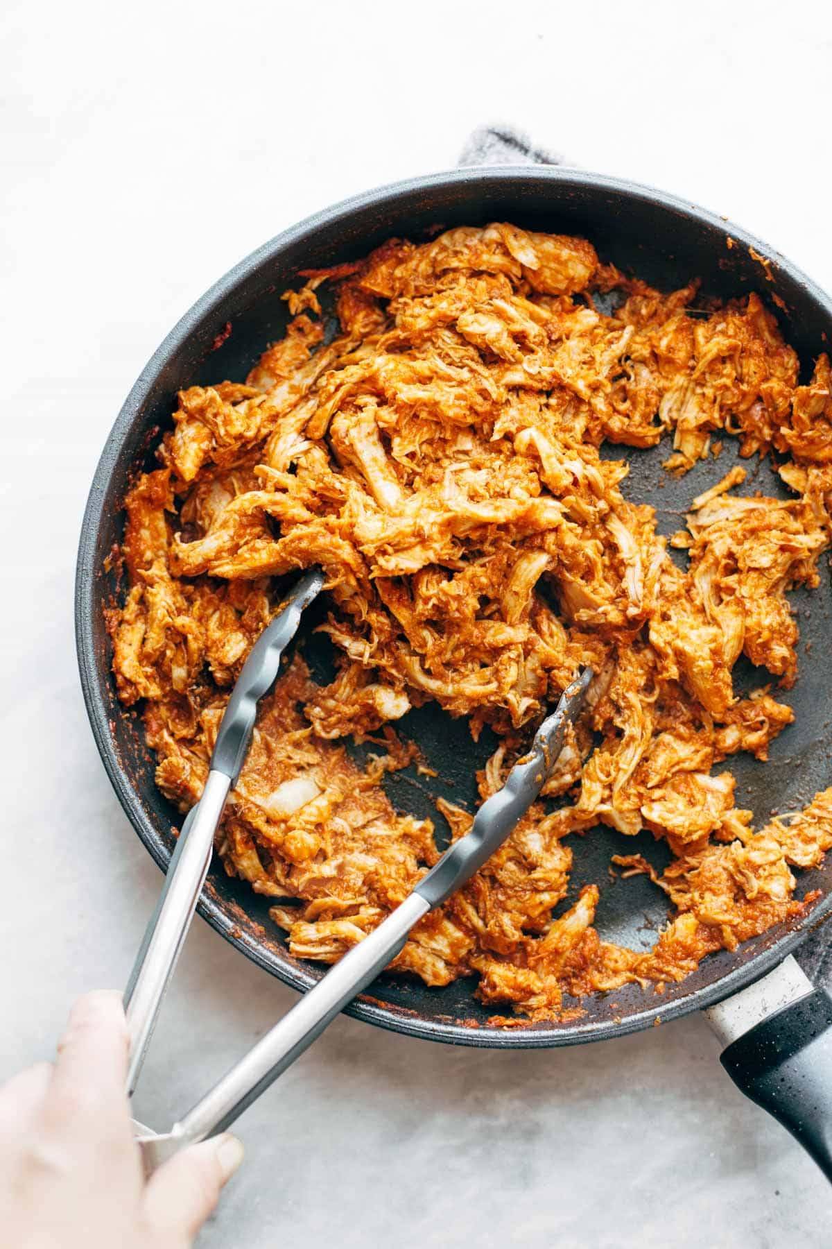 Chicken Tinga in pan with tongs.