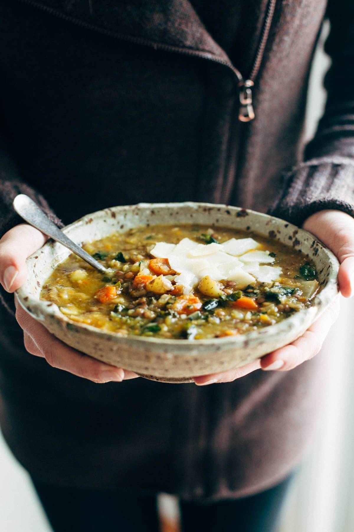 White hands holding a bowl of lentil soup