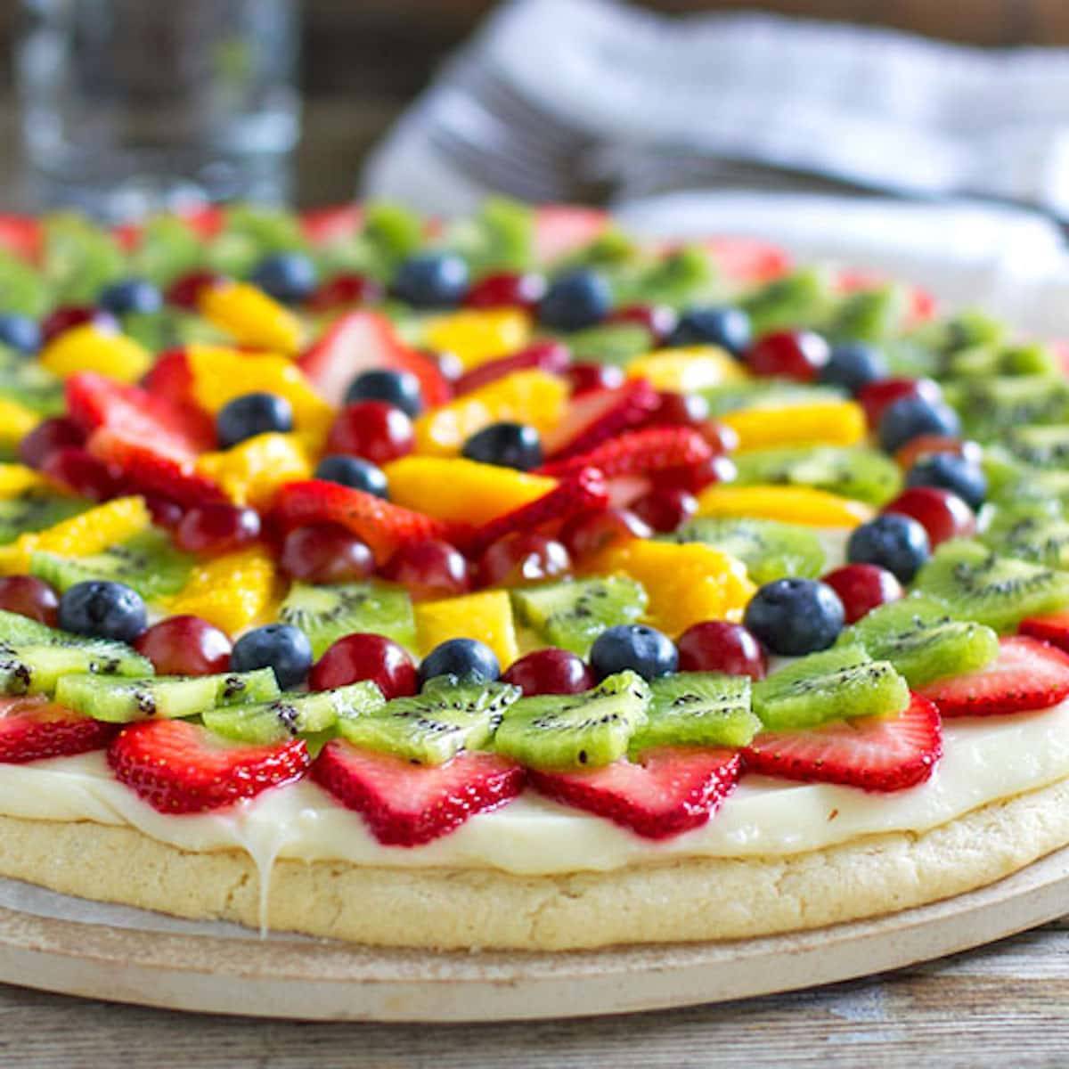 Fruit pizza with a soft sugar cookie crust with a cream cheese frosting and topped with sliced fruit. 