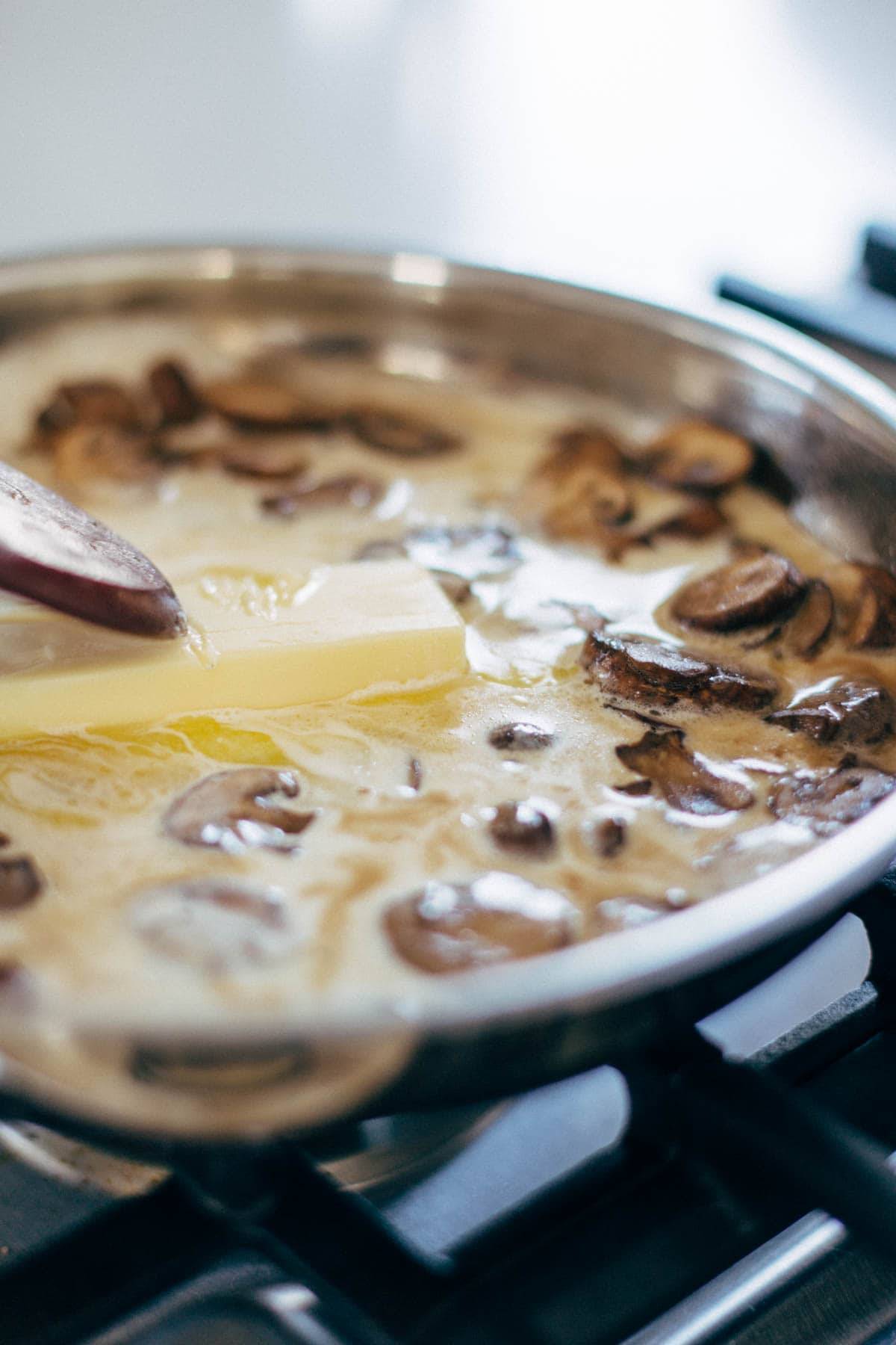 Mushrooms, butter, and heavy cream in pan on stove.